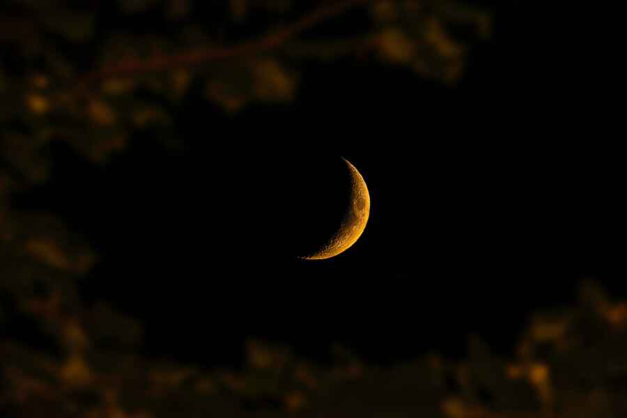 A reddish crescent moon against a black night sky