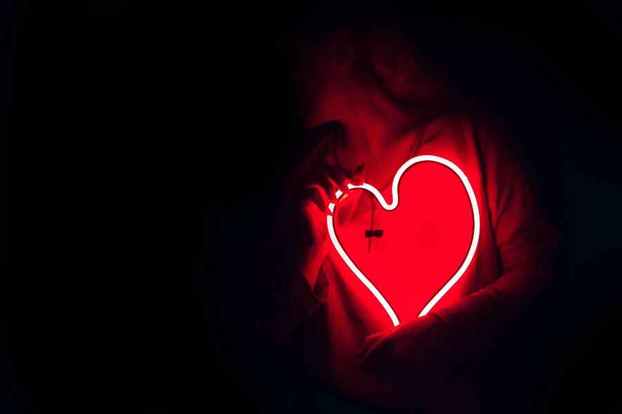 A person holding a large neon red heart in front of herself