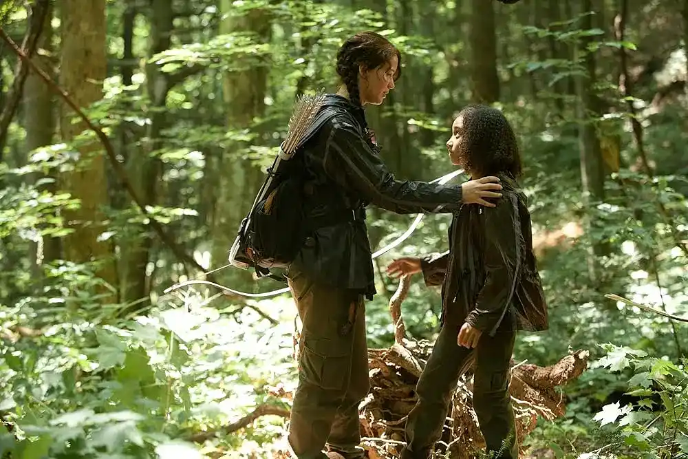 Katniss puts her hand on Rue's shoulder in the forested area of the Hunger Games arena