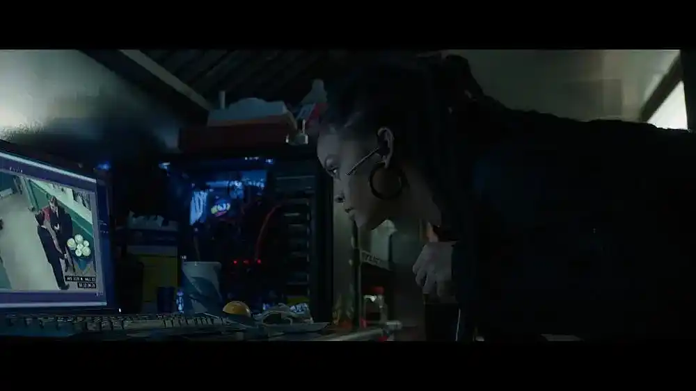 Rihanna leans over a keyboard and monitor showing a security camera feed
