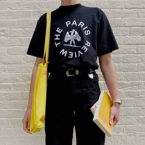 A person wearing a black Paris Review t-shirt with a circular logo.