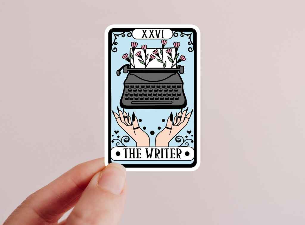 Hand holding up a sticker of a tarot card showing a typewriter and titled 'The Writer'