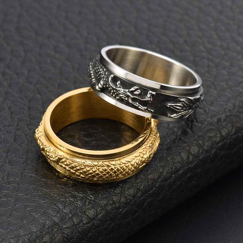 Photo of a pair of rings, one gold and one silver, with ornate dragon details, one laying on top of the other.