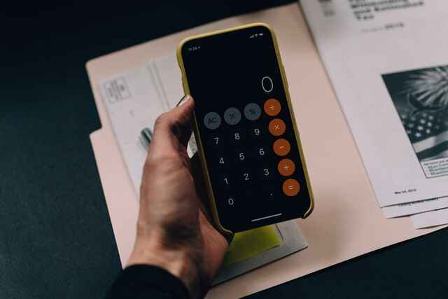 Hand holding an iPhone, with the Calculator app open. The calculator simply says zero.