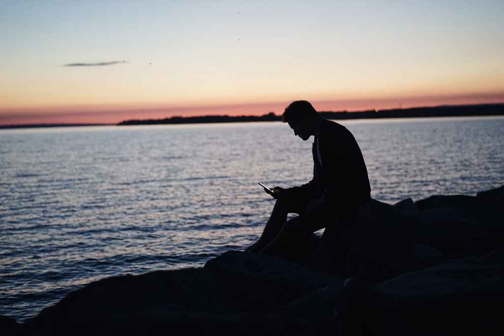 Kindle Vella | Silhouette of a person reading on their phone against the sunset