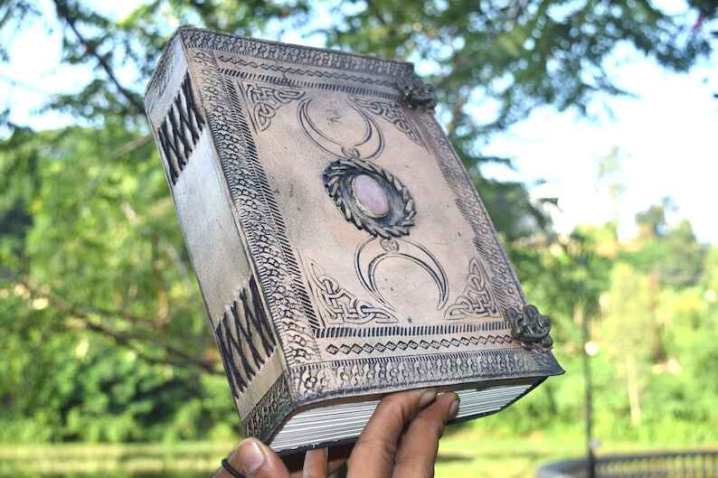 Photo of a leather journal with a rose quartz on the cover, held up in the light in front of trees.