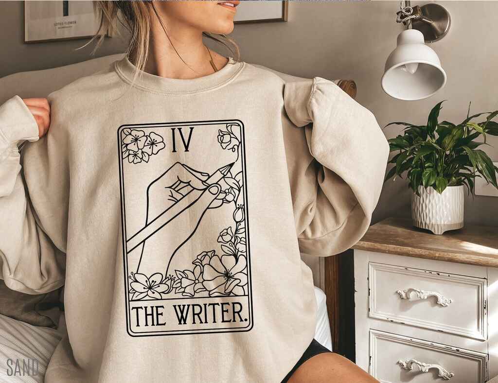 Woman wearing a beige sweatshirt with a 'writer' tarot card desing