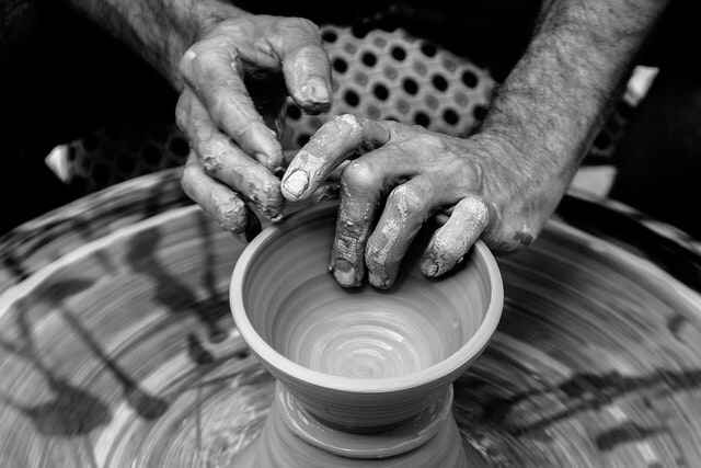 Two hands spin a potter's wheel, in black and white.