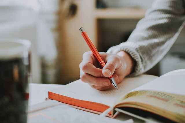 A hand holding a pen writes in a notebook